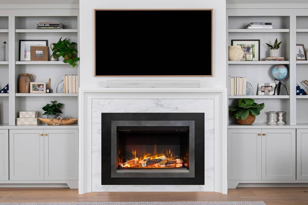 Fireplace with a TV above and built-in white bookshelves on either side, with decorative items on shelves and a glowing fire.