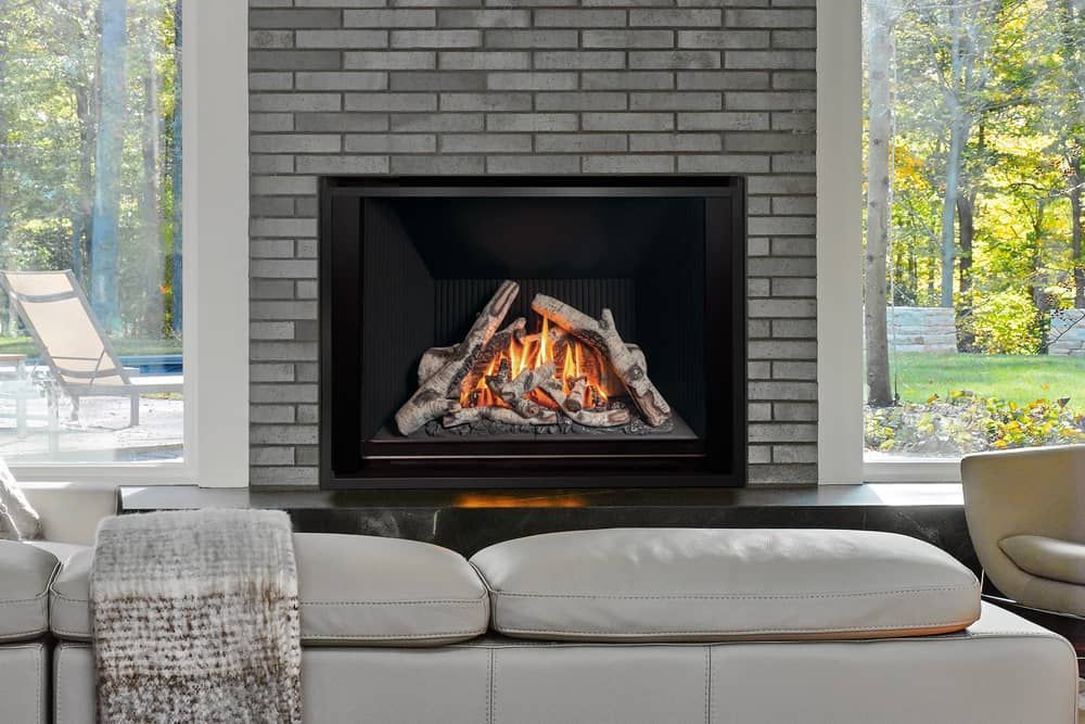 Modern fireplace with faux logs and flames built into a gray brick wall, with a white sofa in the foreground.
