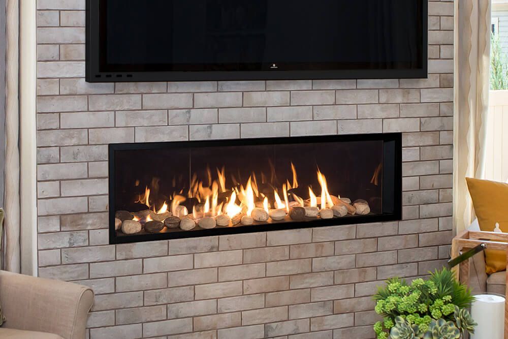 A modern gas fireplace with a lit flame in a brick wall setting, and a TV is mounted above it.