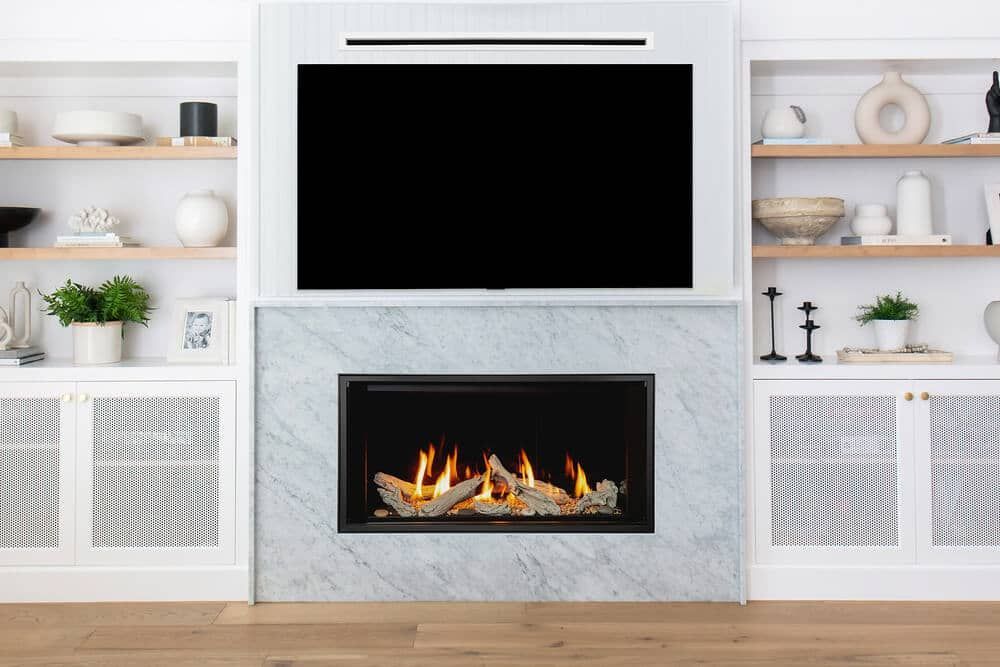 A modern fireplace with a black framed fire, set in a marble surround beneath a large television. Built-in white shelves flank the fireplace.