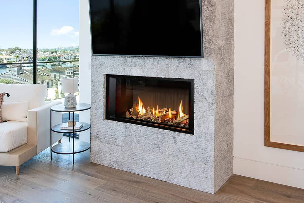 A modern living room features a fireplace with a mounted TV, and a glass side table with a white sofa and a window view.