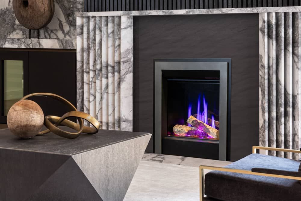 Modern fireplace with blue and purple flames, set in a gray and black stone surround.  Decorative sculptures sit in front of the fireplace.