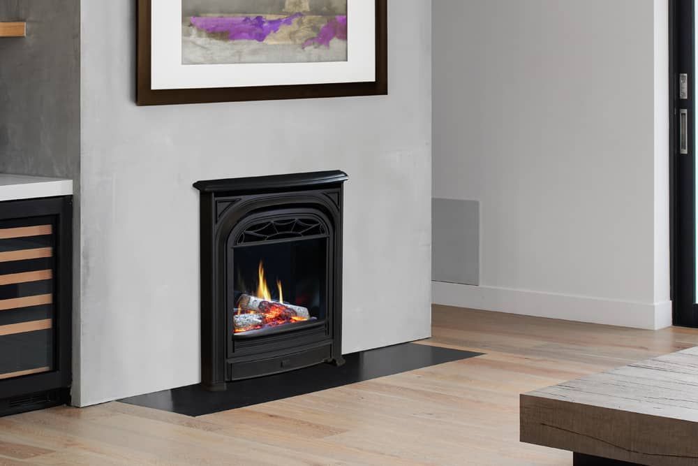 A gas fireplace with a black wrought-iron facade is set into a white wall. Above, a framed abstract painting hangs, with wood flooring.