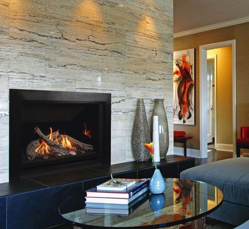 Fireplace with logs, set in a stone wall. In front, a glass table with books and vases, and artwork on the adjacent wall.