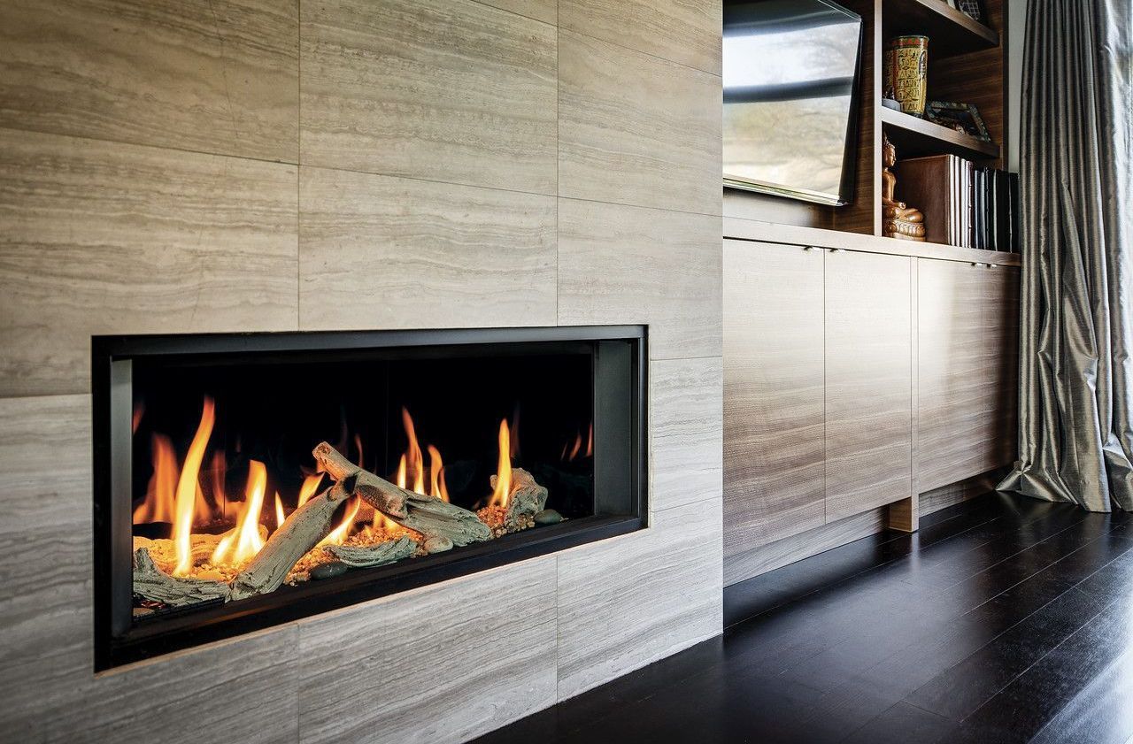 Modern fireplace with flames and logs set in a stone wall, next to a wooden cabinet and dark floor.