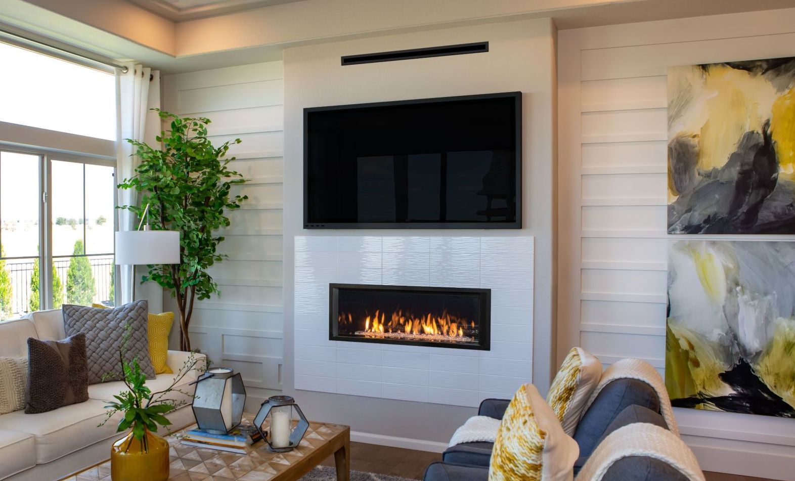 Living room with white fireplace, large TV, and artwork. A couch and coffee table are in the foreground.
