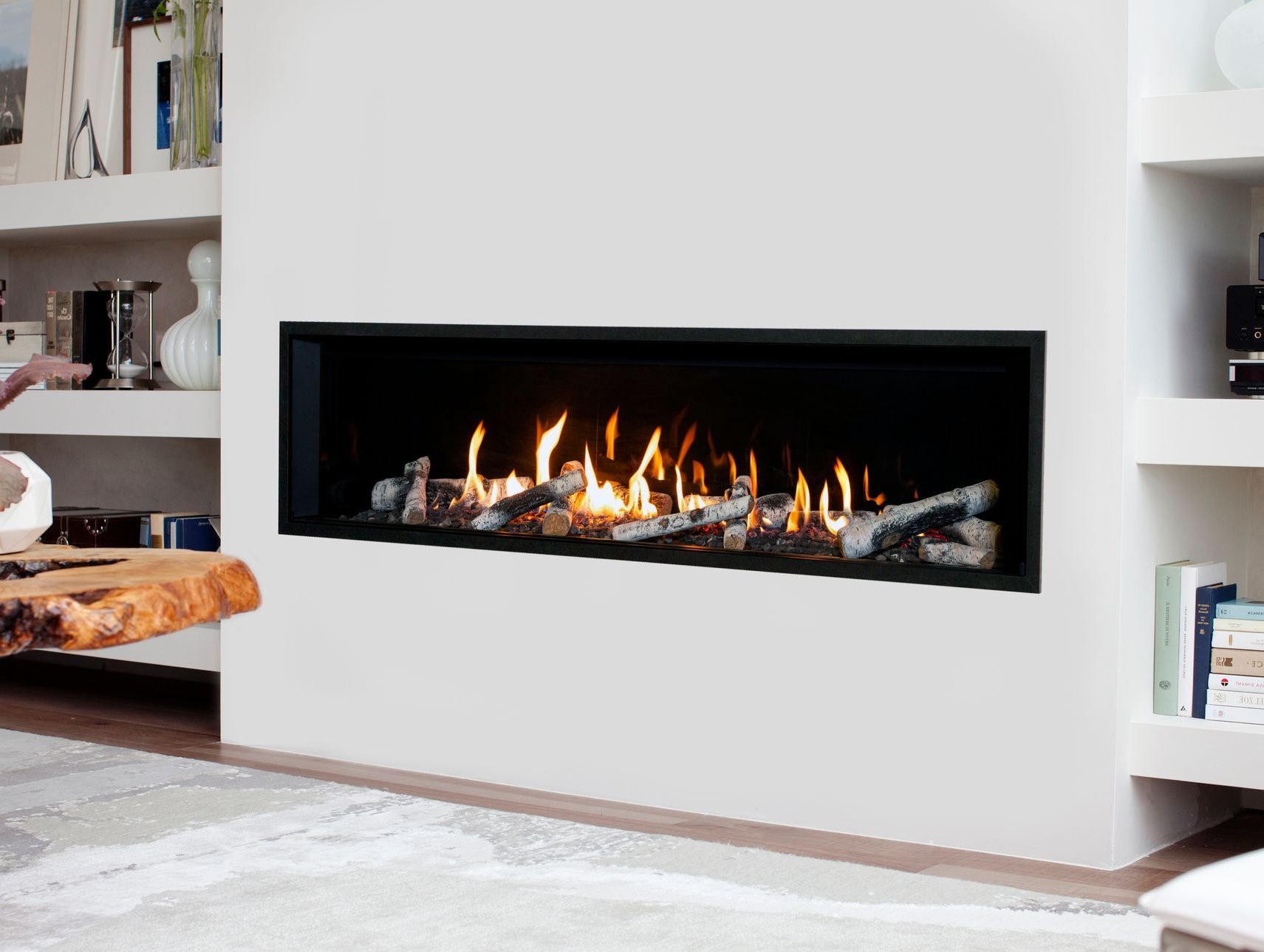 A modern, linear fireplace with flames burning in a white-walled room, flanked by built-in shelves.