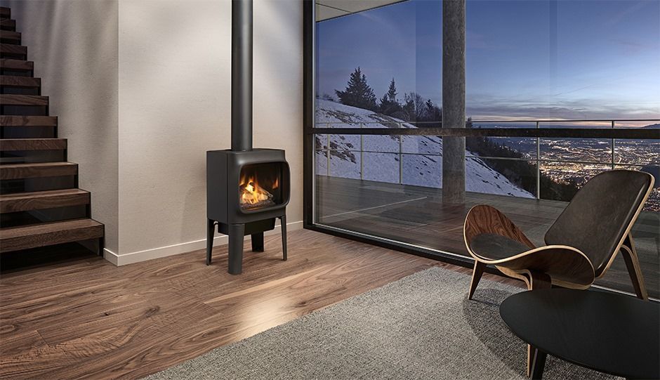 A modern living room with a lit fireplace, wooden floors, a view of snow-covered mountains, and a mid-century modern chair.