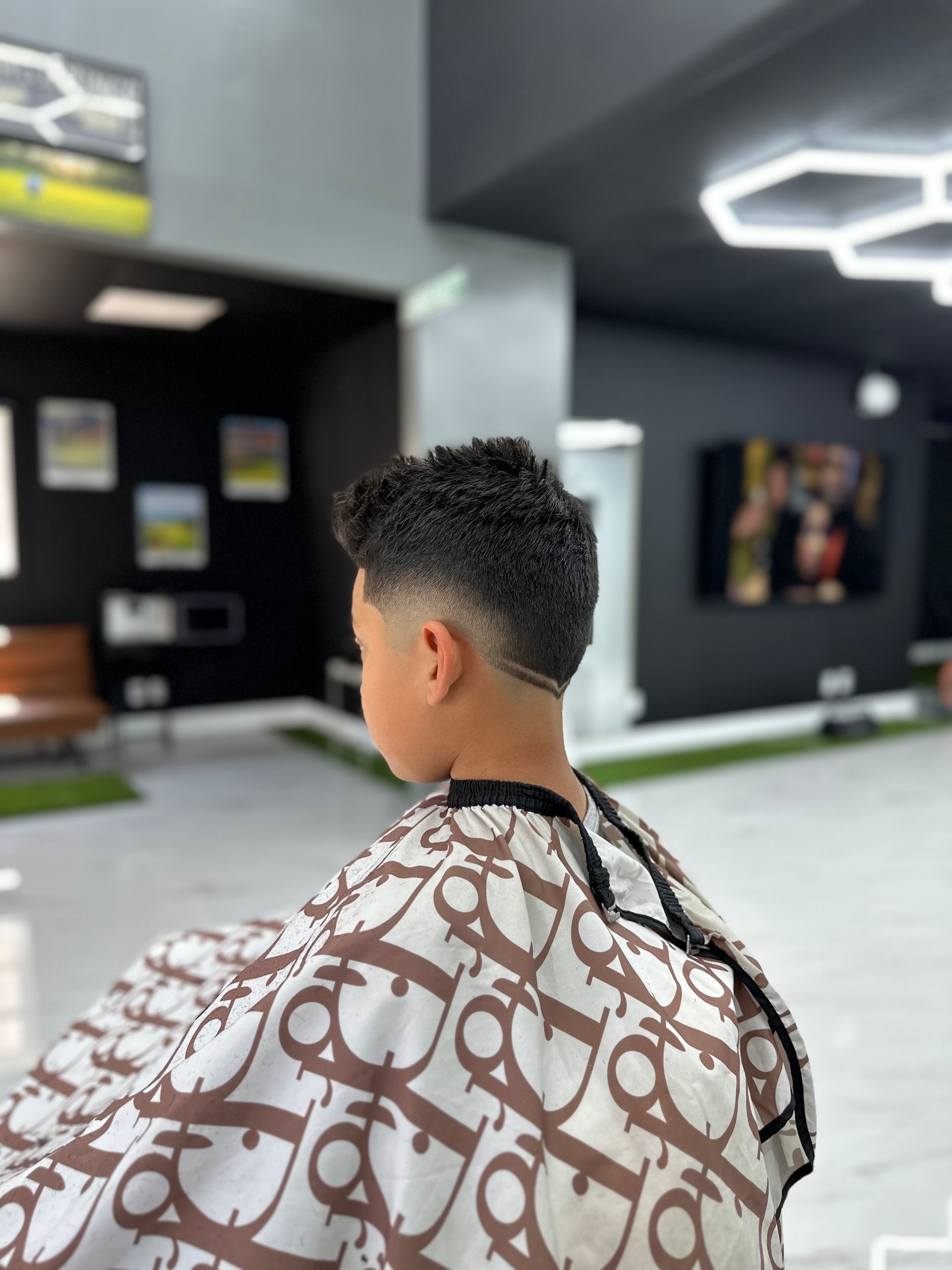 Person with short curly hair sits in a barbershop wearing a patterned cape, viewed from behind.