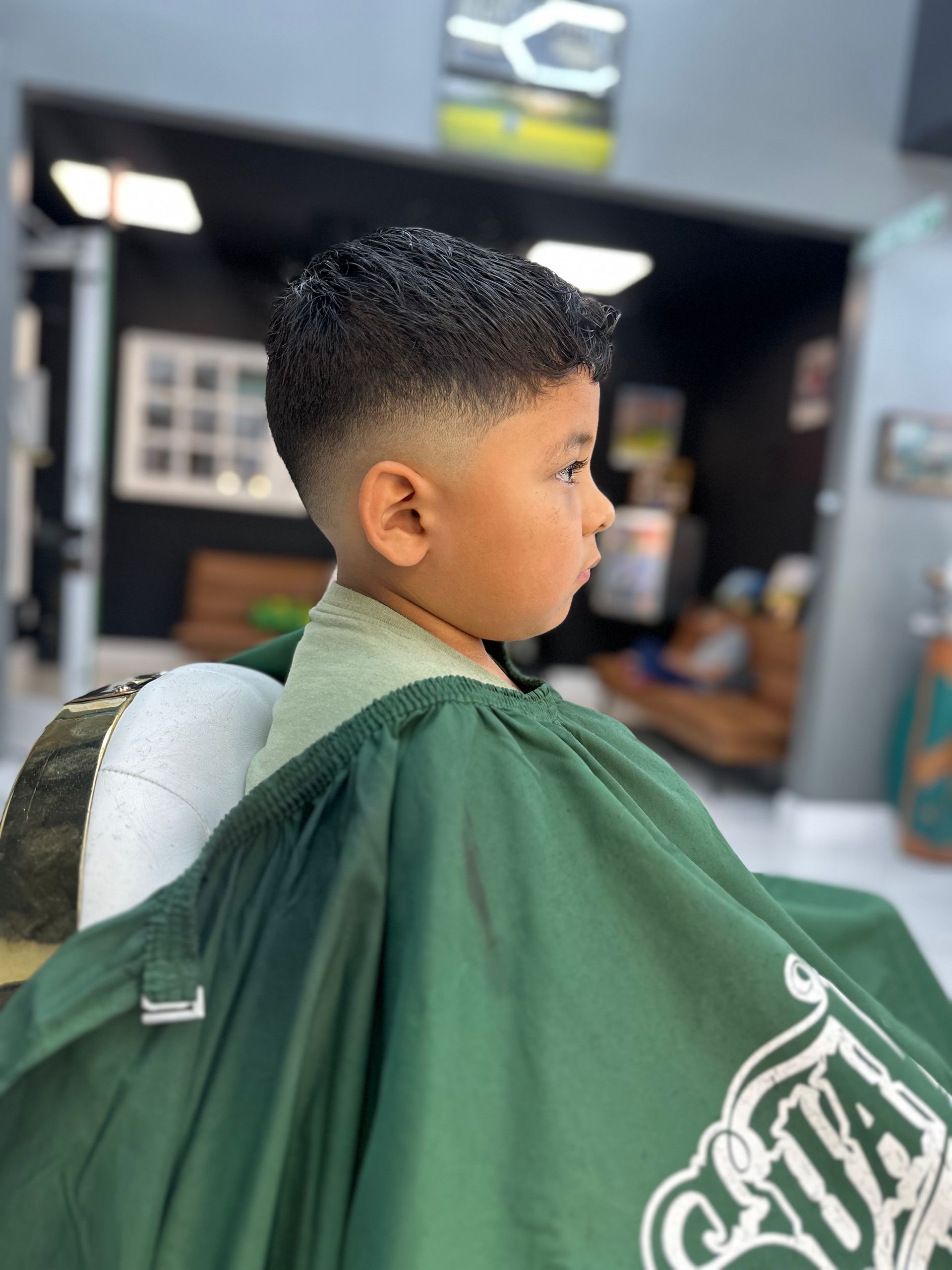 Child in a barber cape getting a haircut, shown in side profile at a barbershop.