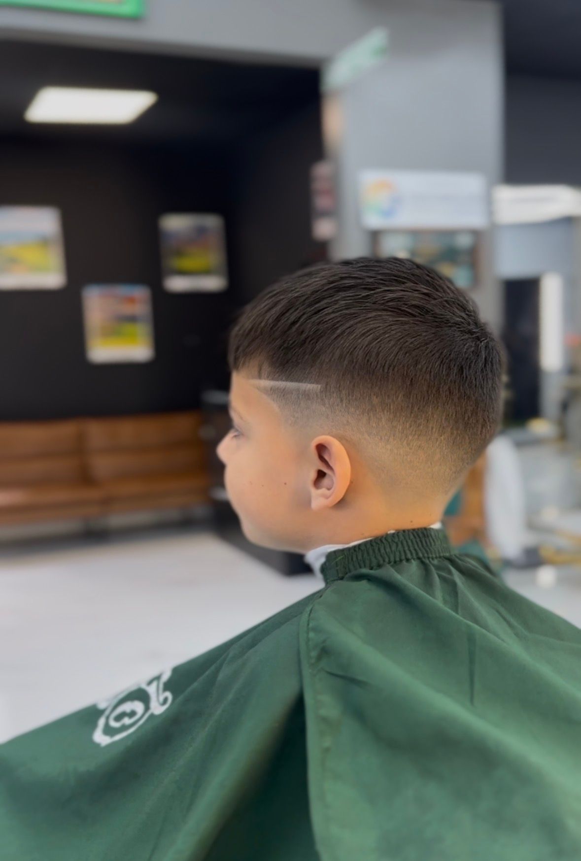Child with a fresh fade haircut wearing a green barber cape in a barbershop