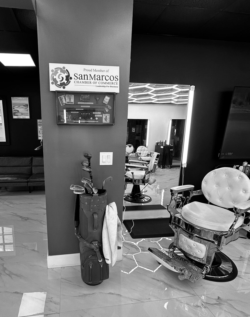 Barbershop interior with a mirror, barber chair, hair tools, and a small display sign by the counter.