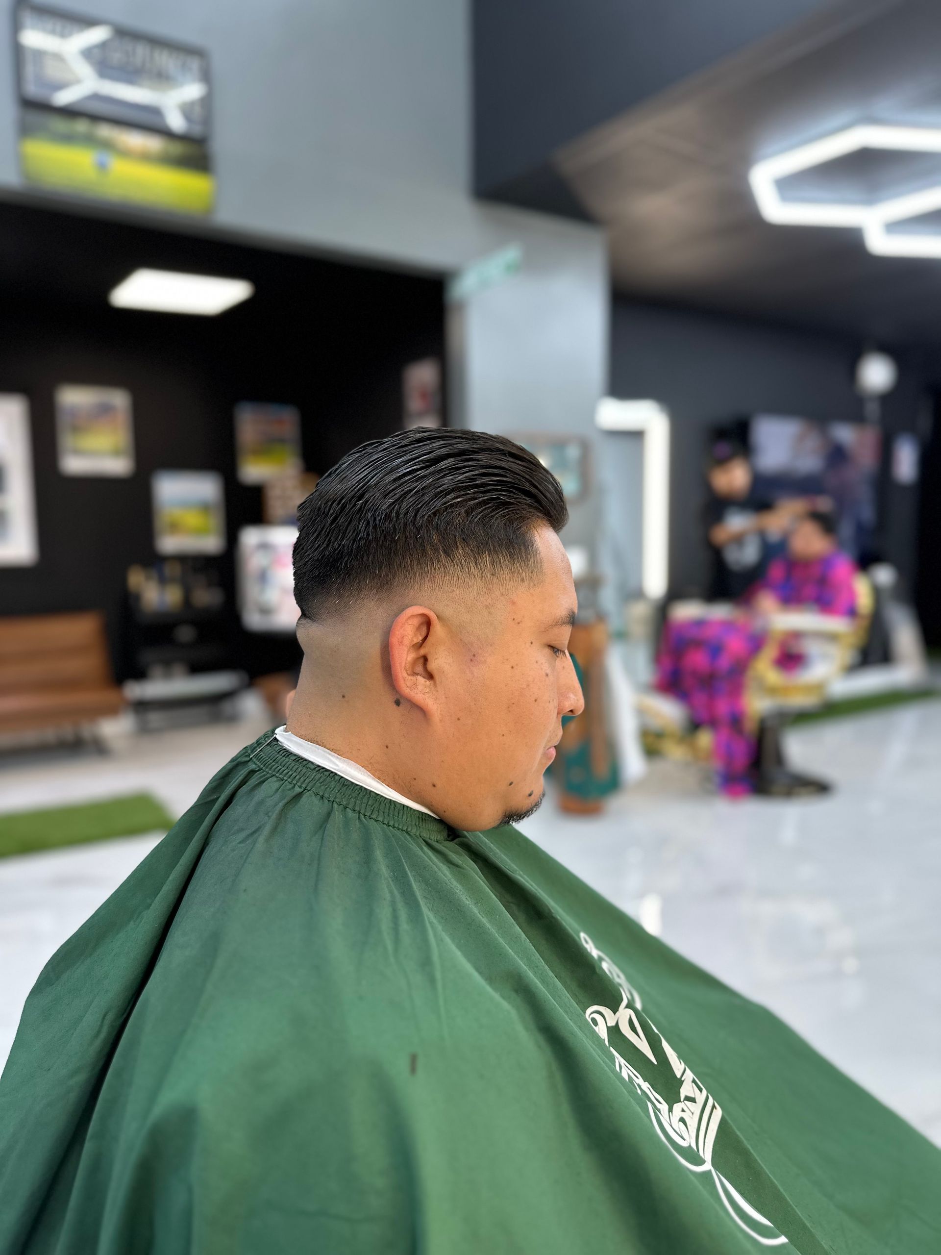Man in green barber cape getting a haircut in a modern barbershop