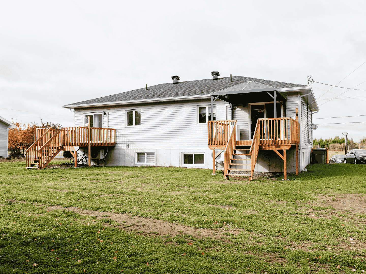 Une maison blanche avec une terrasse en bois et des escaliers est située au sommet d'un champ verdoyant luxuriant.