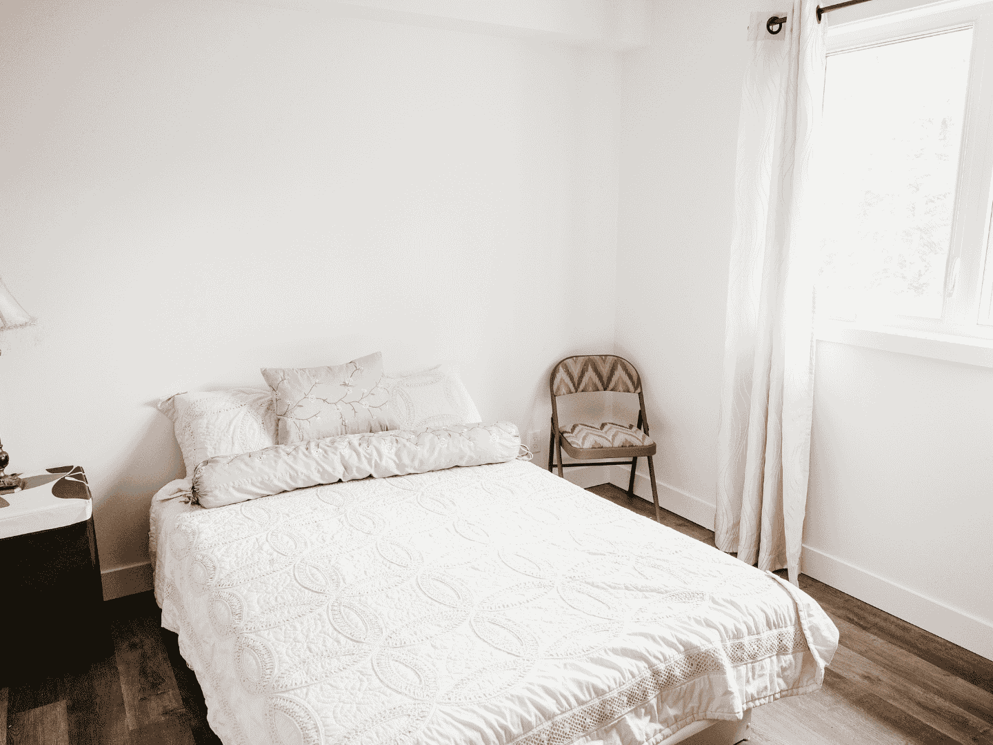 Une chambre avec un lit, une chaise, une table de chevet et une fenêtre.