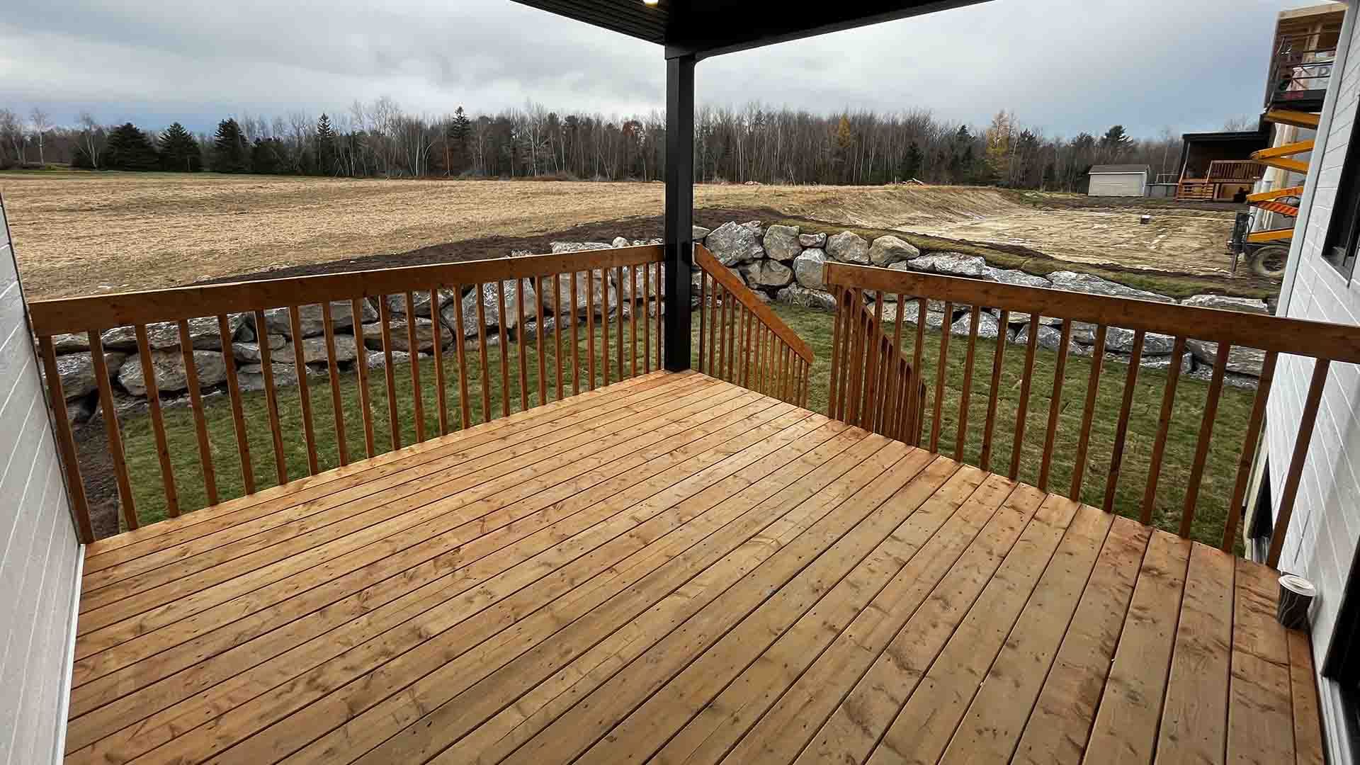Une terrasse en bois avec une balustrade et une vue sur un champ.