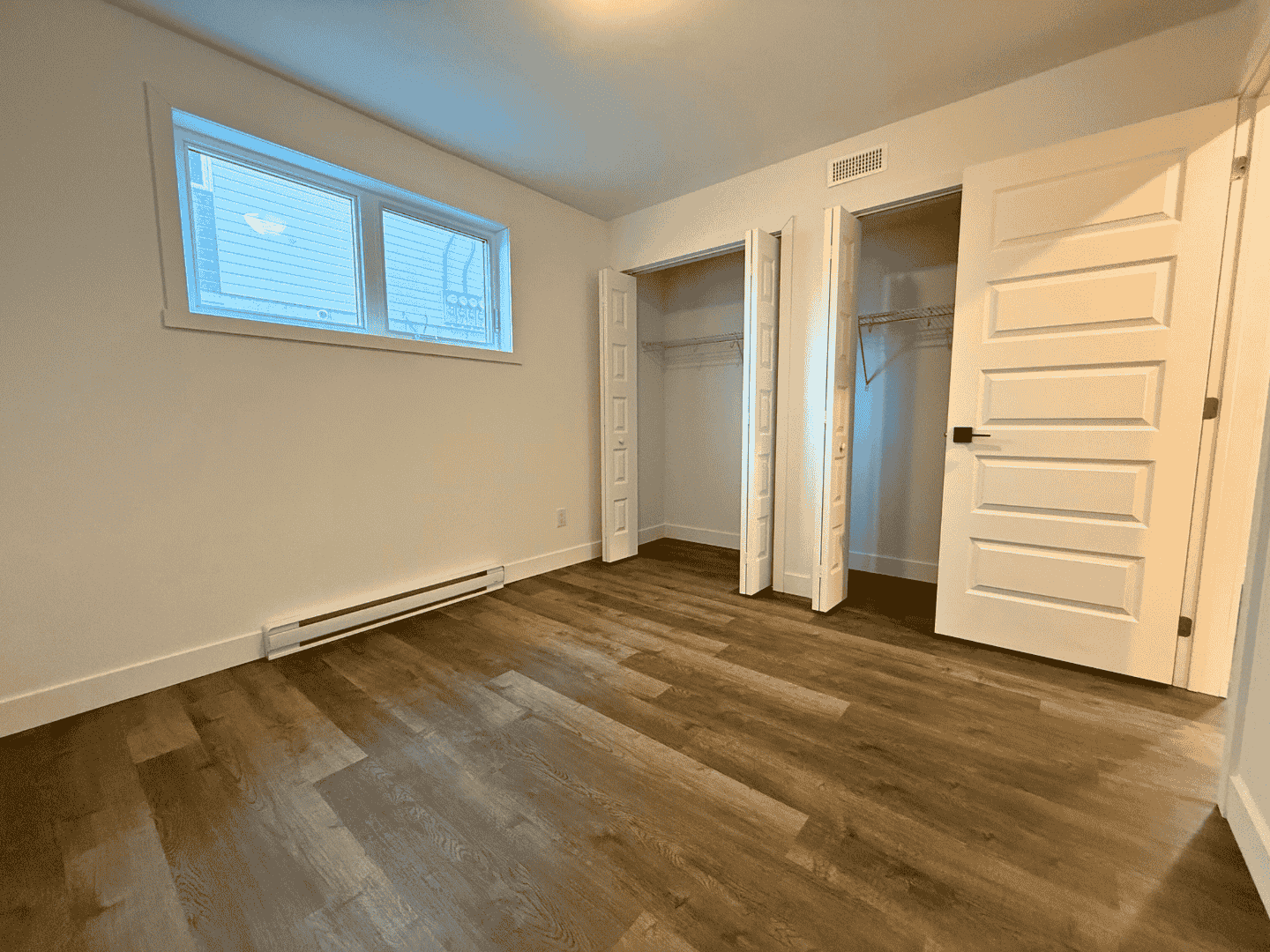 Une chambre vide avec parquet et deux placards.