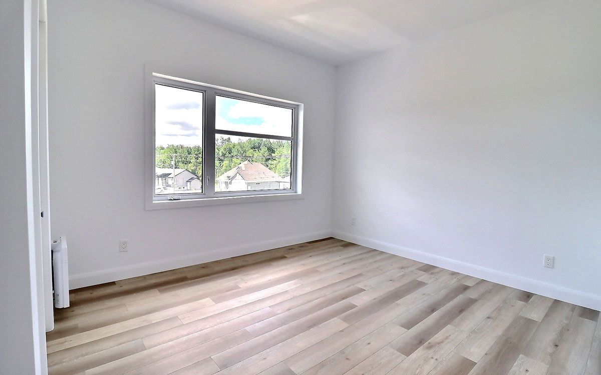 Une chambre vide avec du parquet et une grande fenêtre.