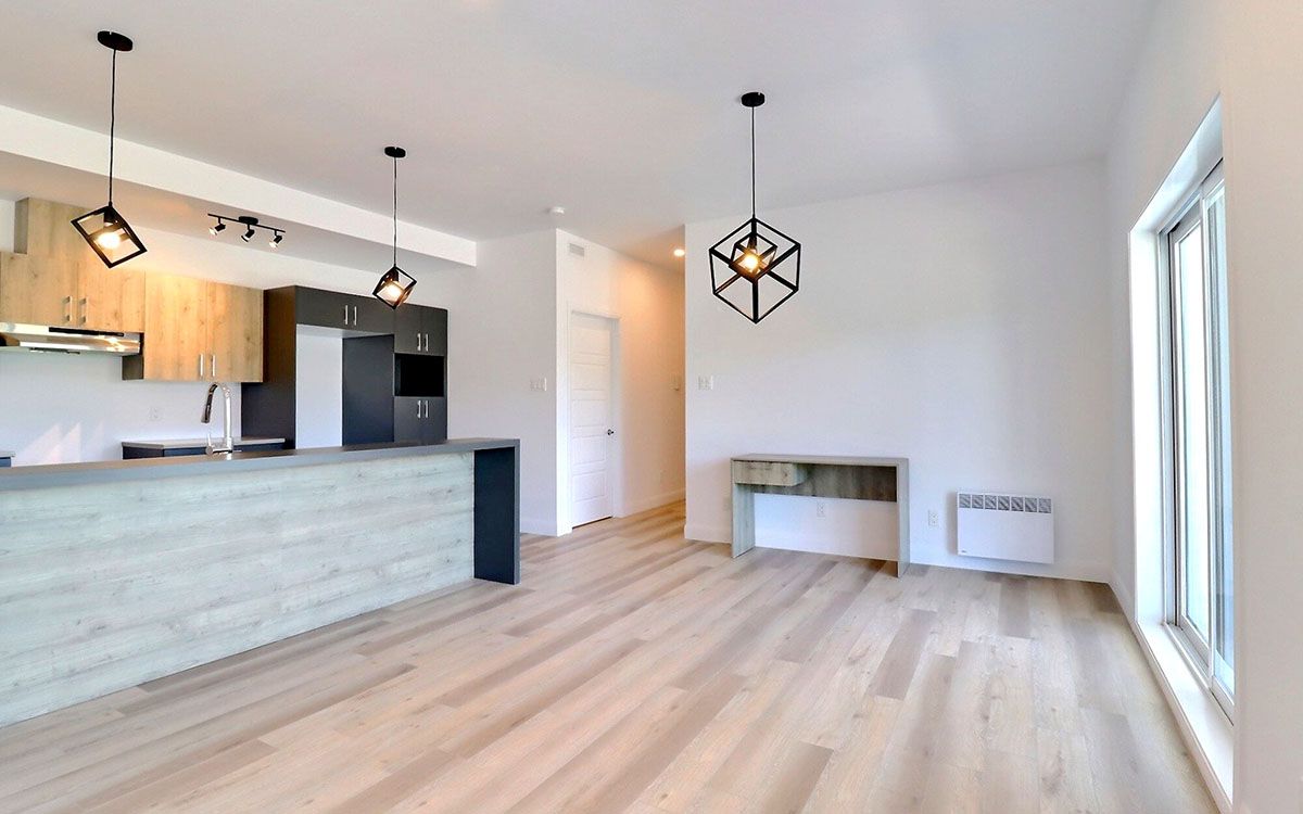 Un salon avec parquet et une cuisine en arrière plan.