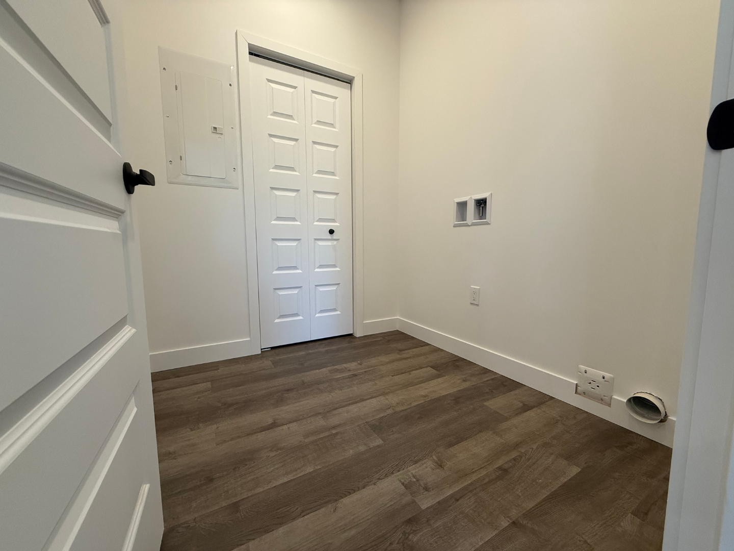 Une pièce avec un plancher en bois, des murs blancs et une porte.