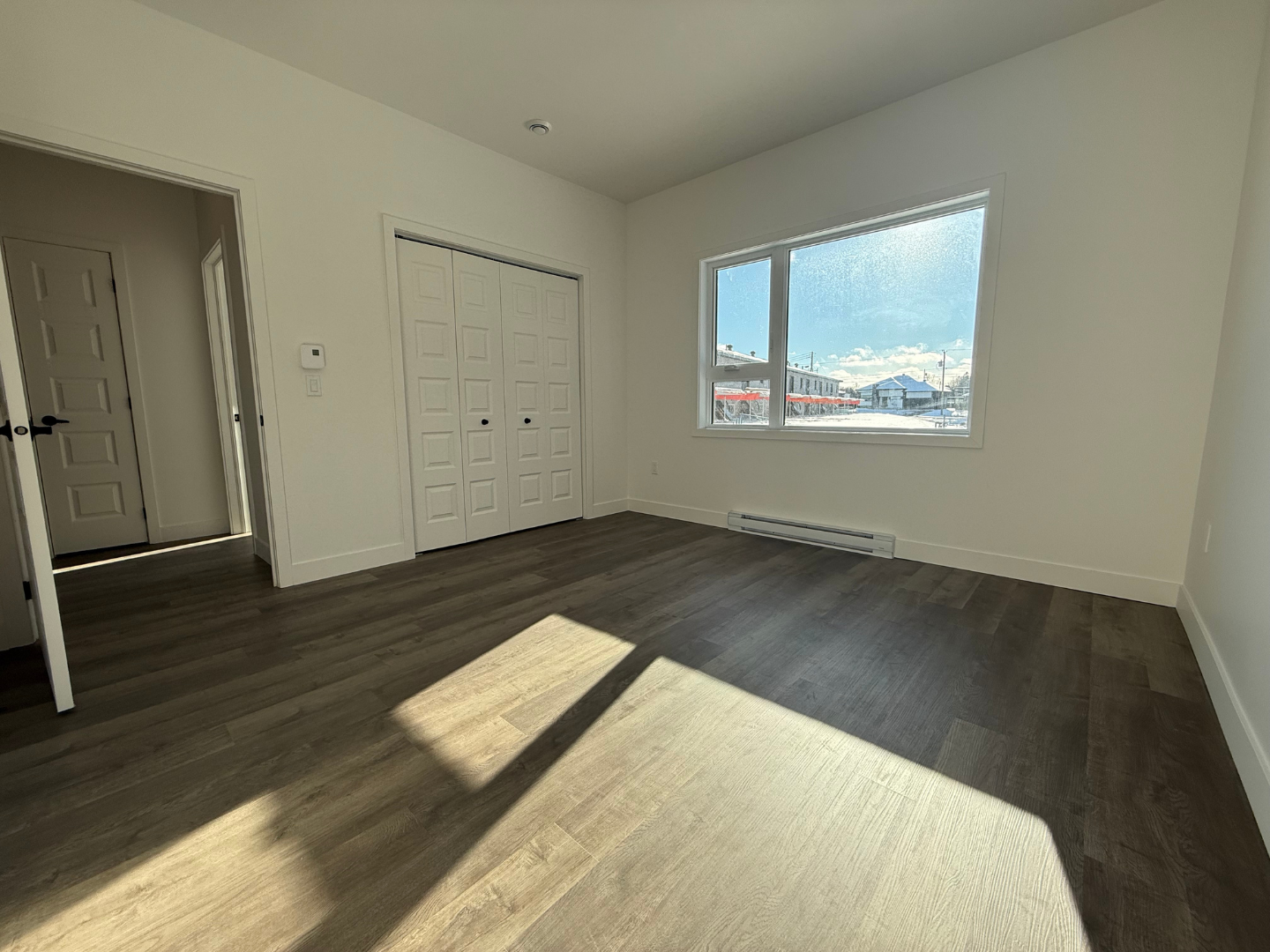 Une chambre vide avec du parquet et une grande fenêtre.