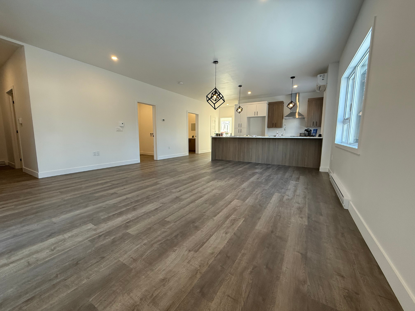 Un salon vide avec du parquet et une cuisine en arrière-plan.