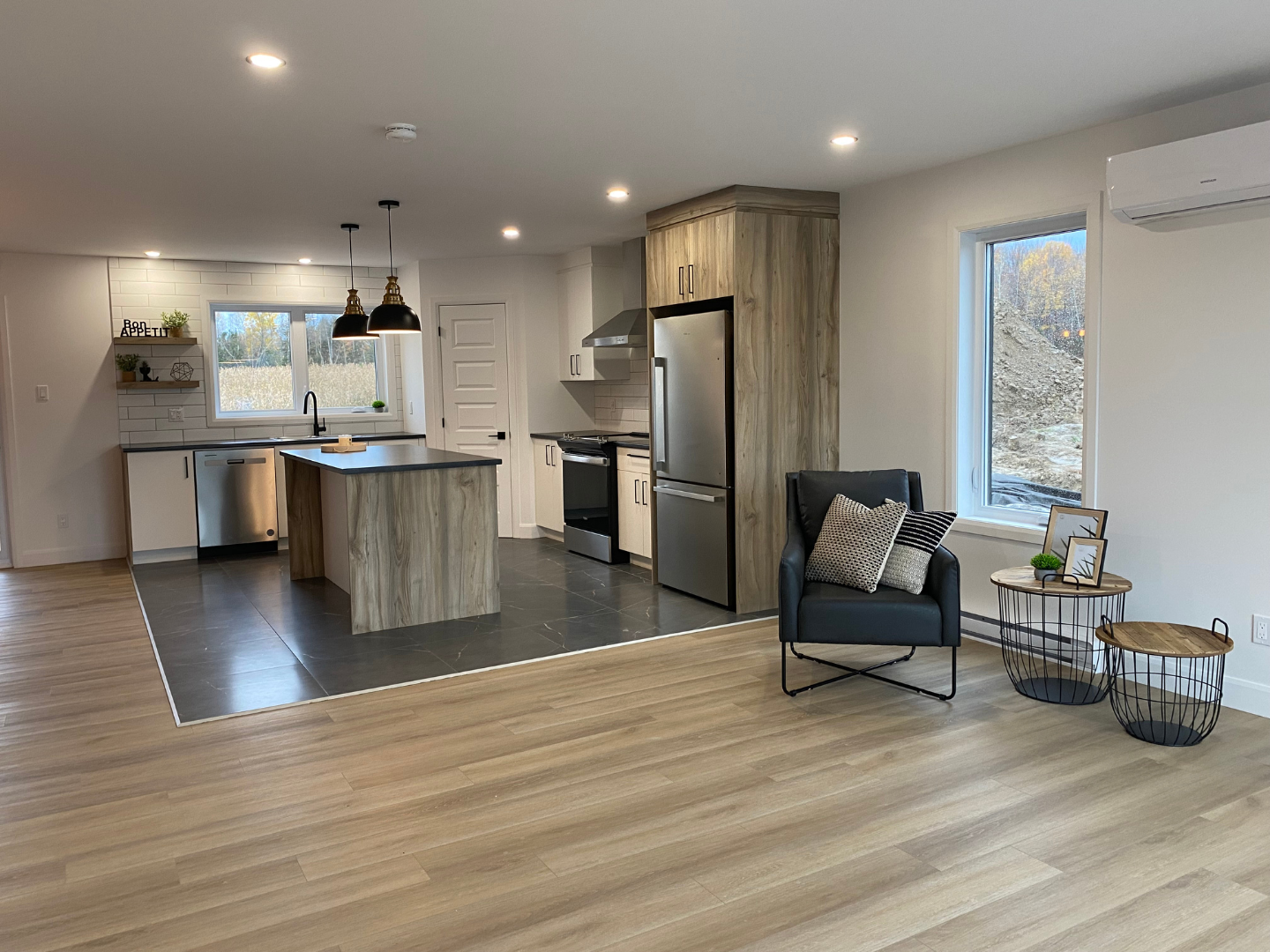 Un salon avec parquet et une cuisine en arrière plan.