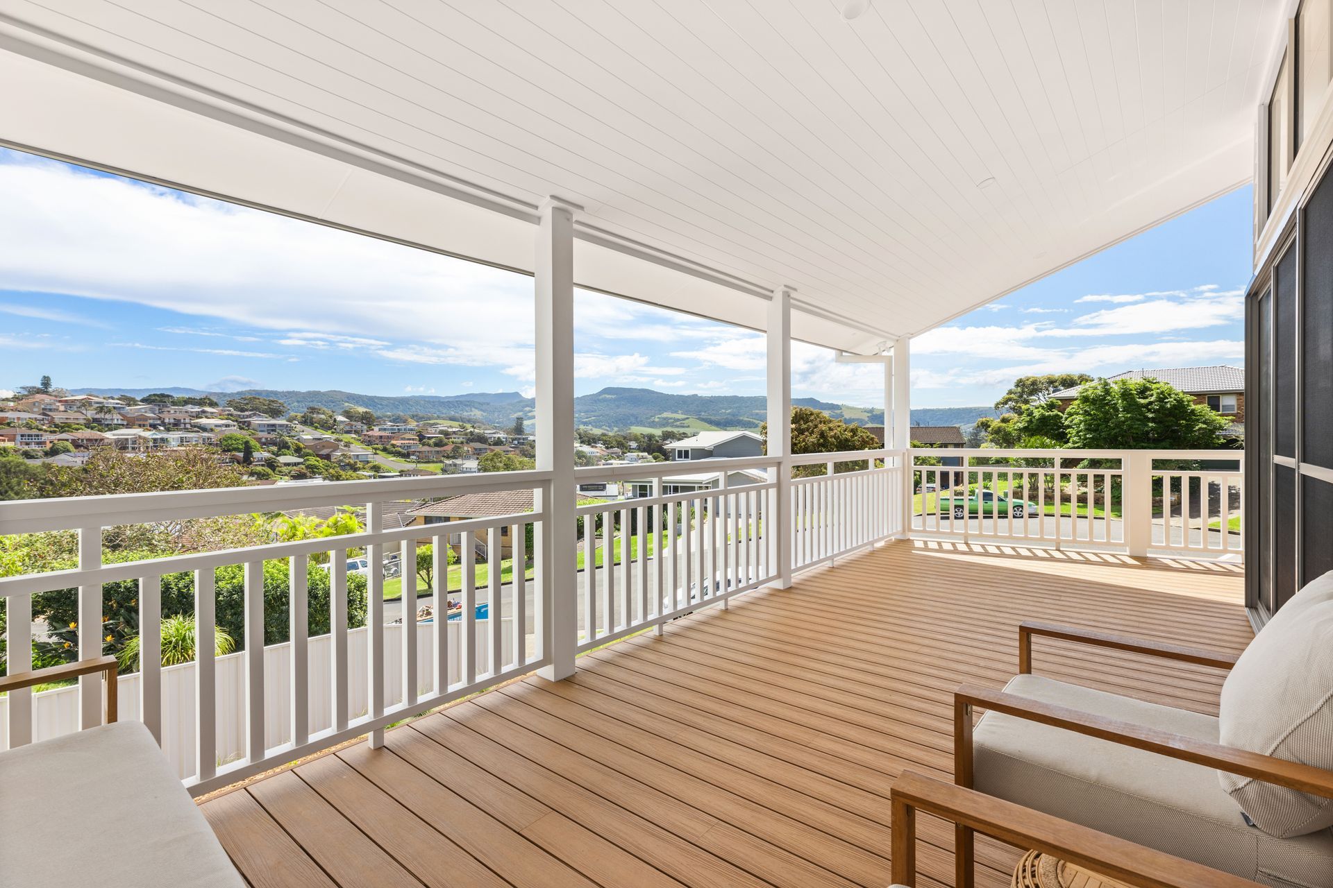 Wooden deck with white railing and ceiling, overlooking a cityscape and distant hills.