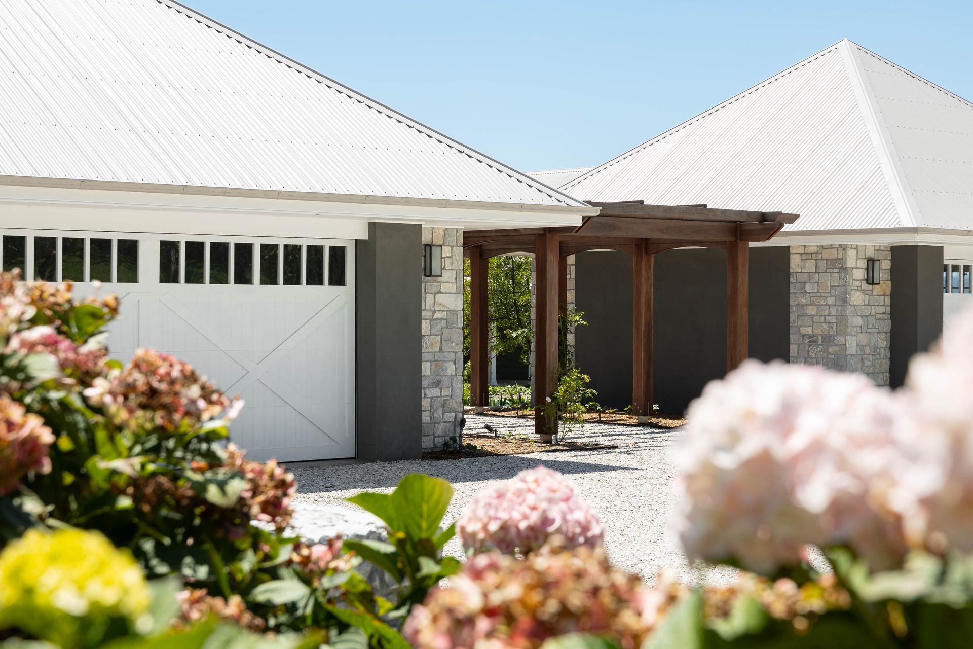 White building with garage, stone accents, wooden pergola, and blooming hydrangeas.
