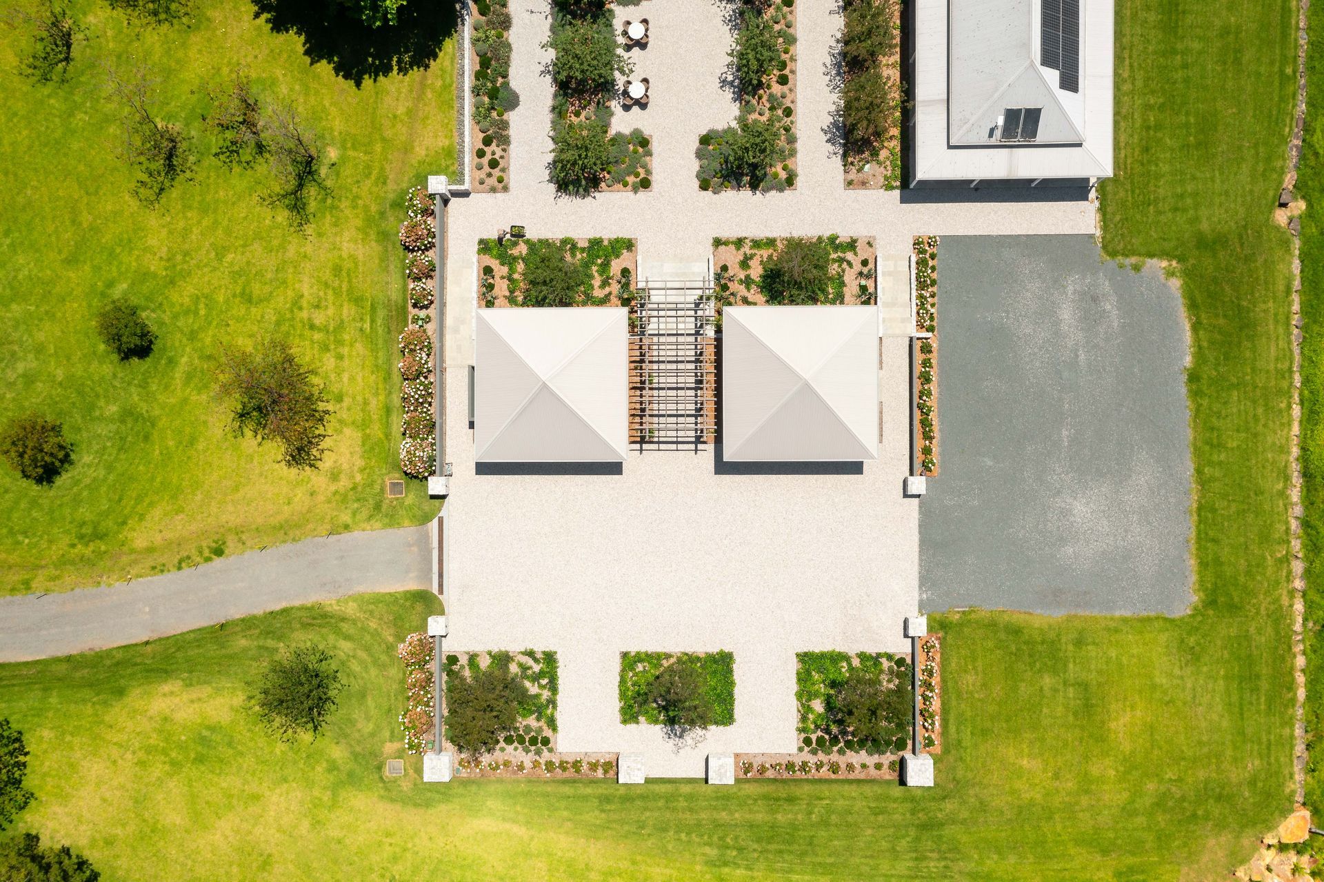 Overhead view of a manicured landscape with buildings, paved areas, gardens, and green grass.