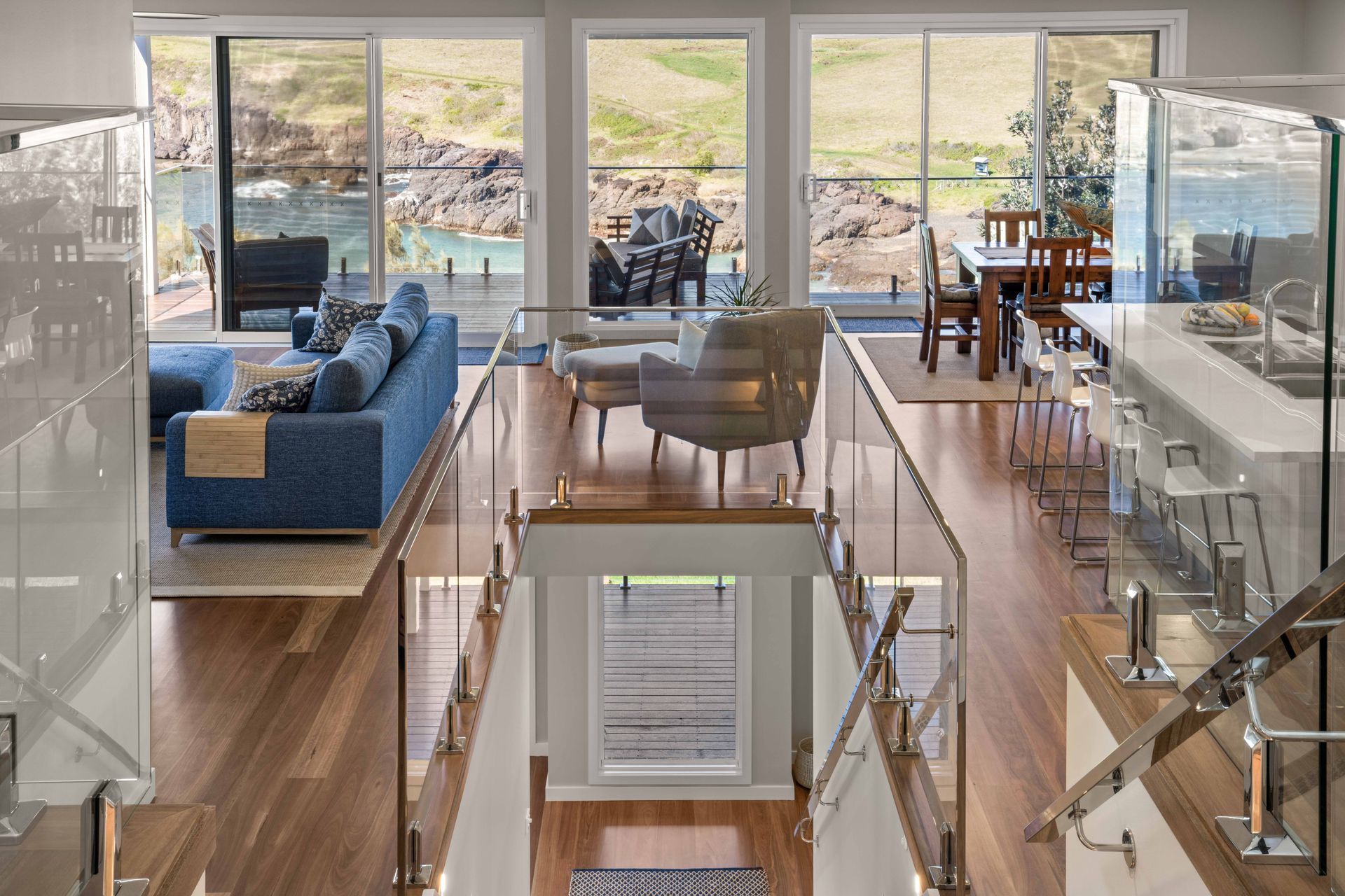 Bright, open living space with glass railings, hardwood floors, and large windows overlooking a scenic waterfront view.