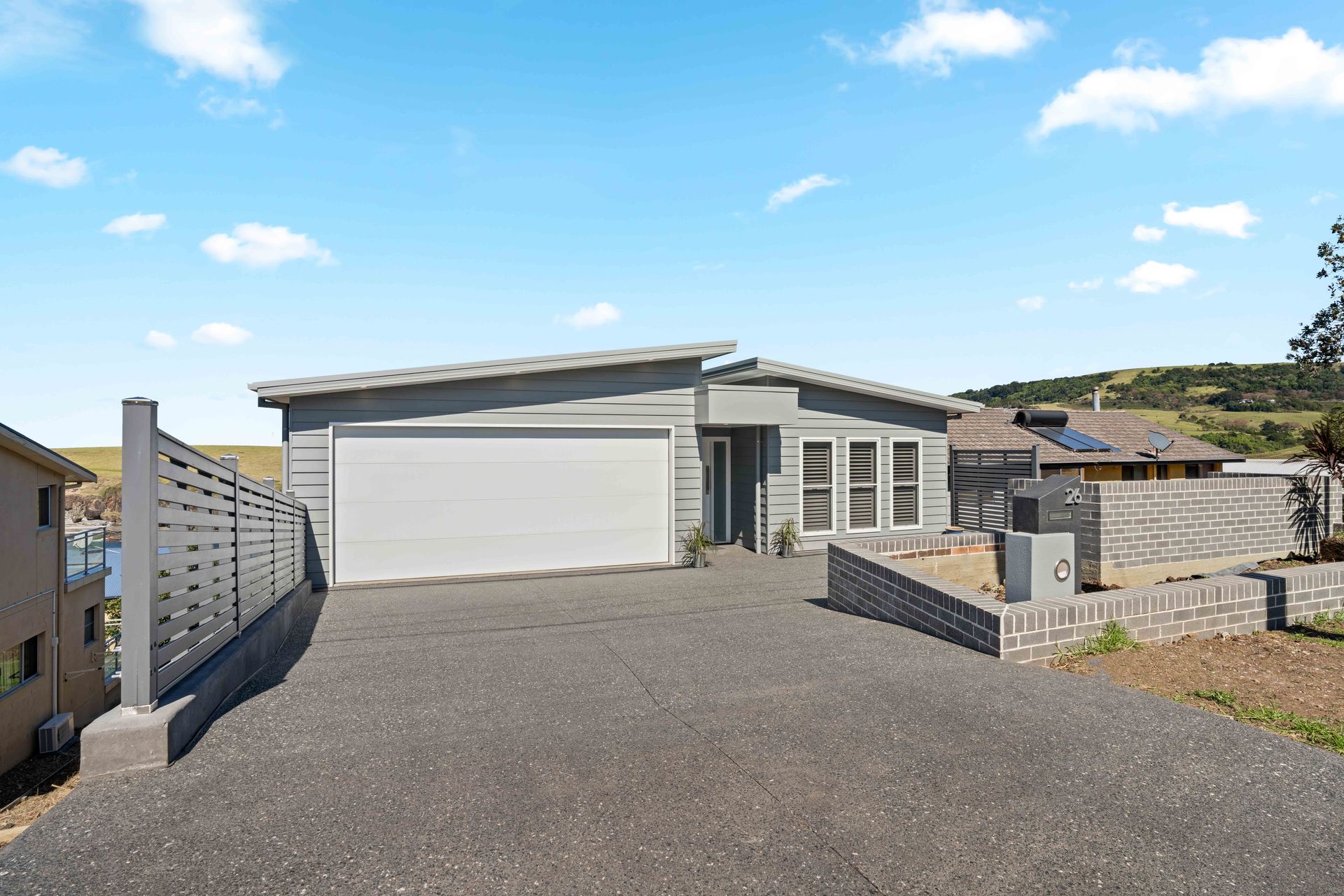 Gray modern house with driveway, garage, and a low brick wall, under a blue sky.