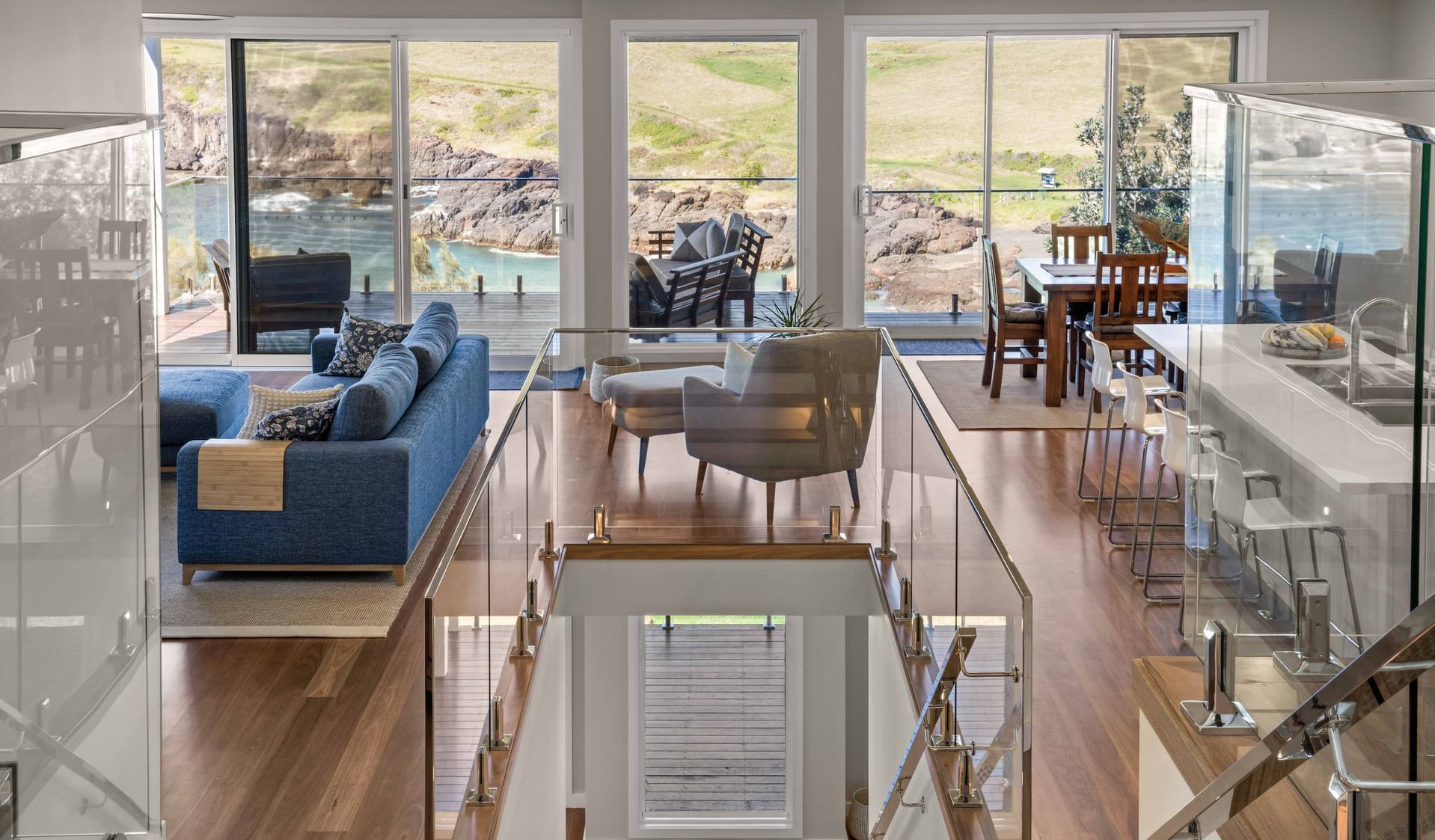 Modern living room with blue sofa, armchairs, and dining area, overlooking a coastal view.