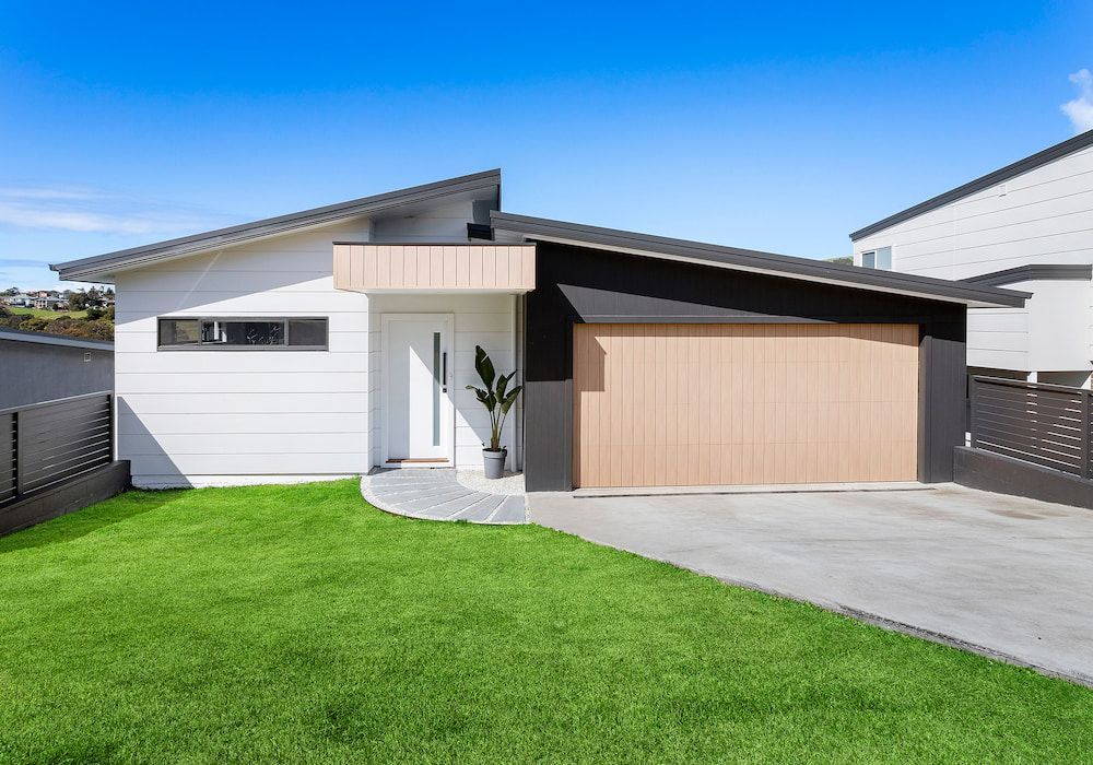 Modern white house with a tan garage door on a green lawn under a blue sky.