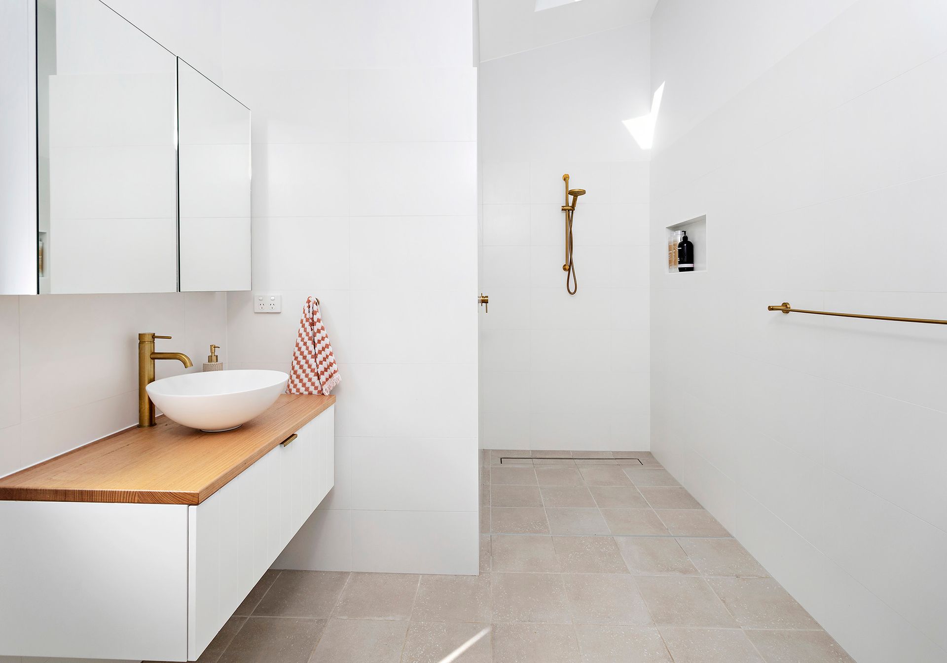 White modern bathroom with wood vanity, gold fixtures, shower, and tile floor.