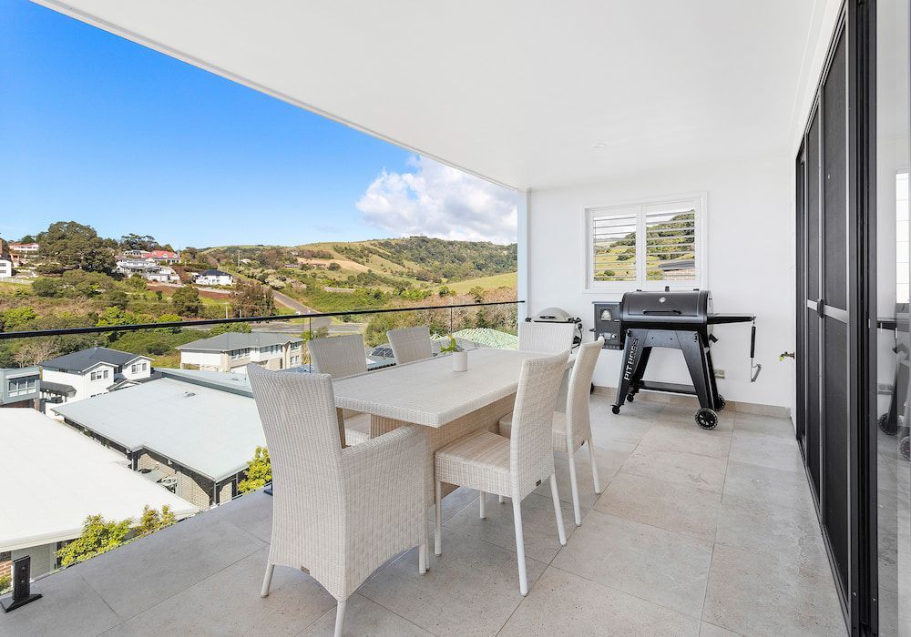 Outdoor dining area with a white table and chairs, a grill, and a scenic view of a hillside.