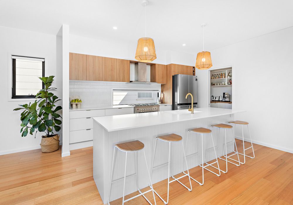 Modern kitchen with wood cabinets, white island, bar stools, and pendant lights.