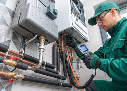 Technician inspecting industrial HVAC piping with a handheld meter in a mechanical room
