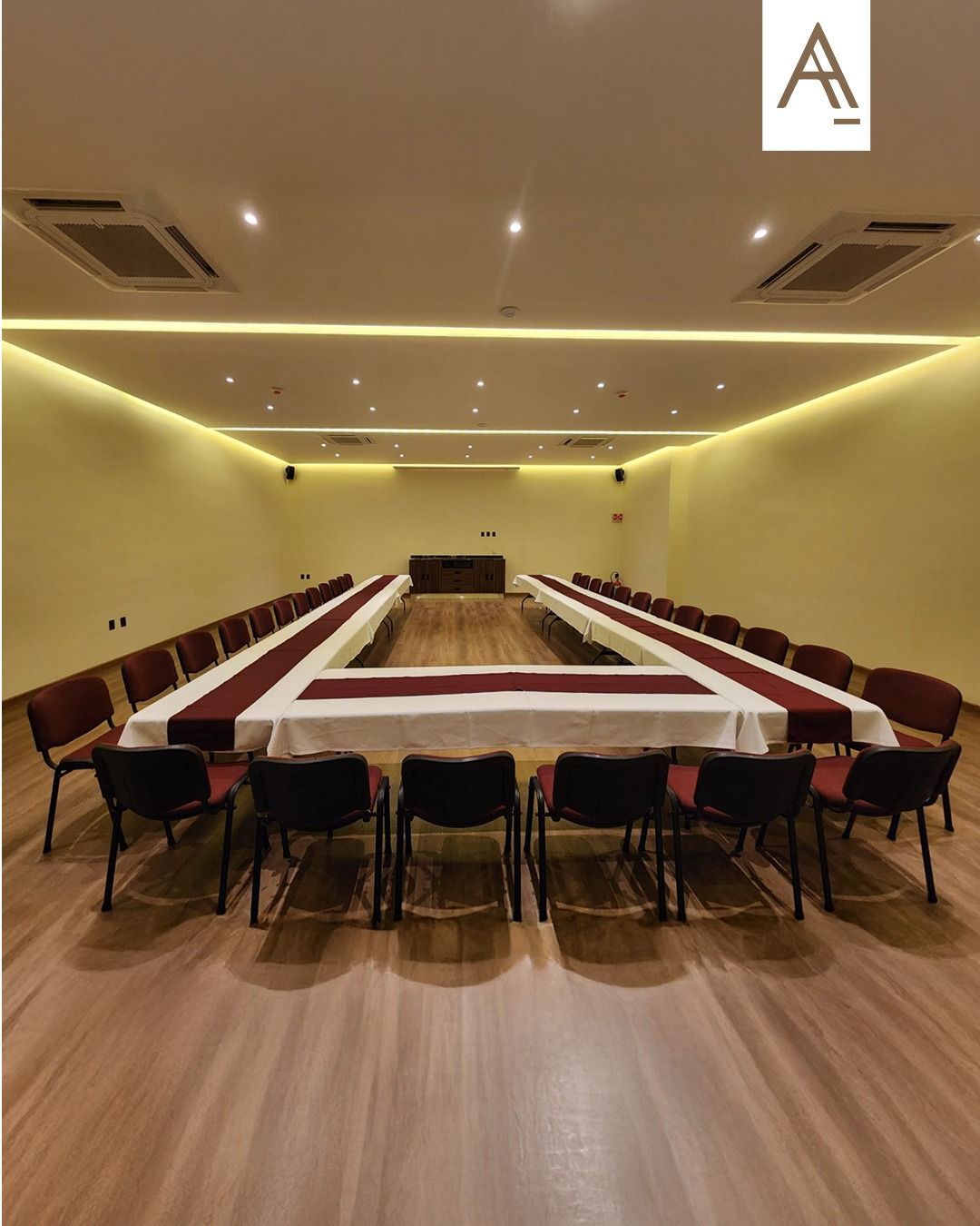 Mesa de conferencias vacía en forma de U en una sala de reuniones moderna con suelo de madera e iluminación amarilla cálida.