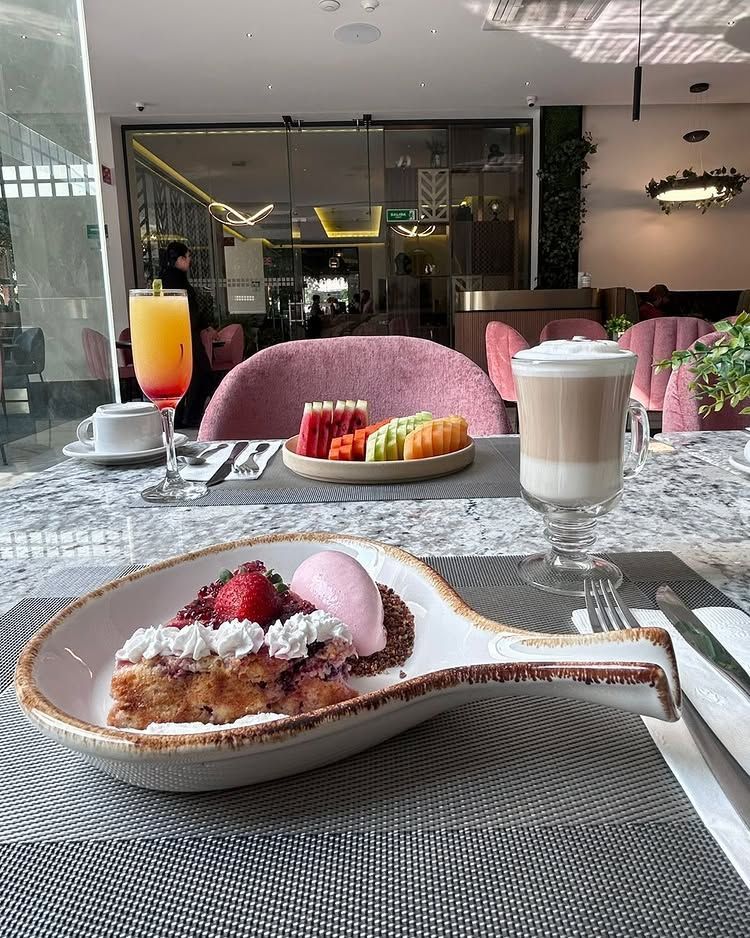 Plato de postre con helado rosa en una cafetería, con bebidas y bandejas de fruta en la mesa.