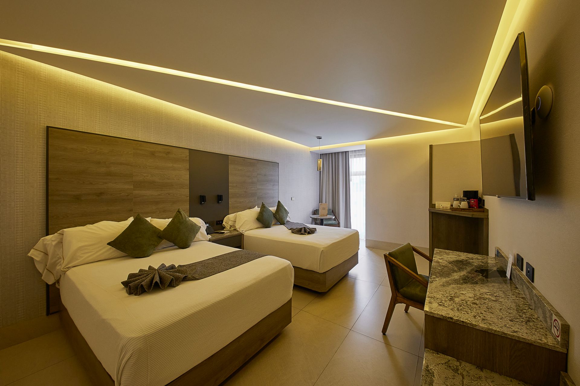 Dormitorio moderno con dos camas bien hechas, detalles en gris verdoso y una ventana luminosa con cortinas.