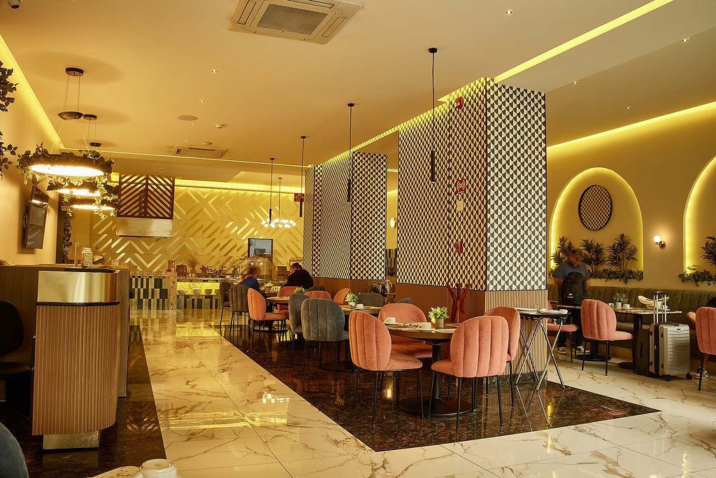 Elegante interior de restaurante con iluminación dorada, sillas rosas y separadores estampados.