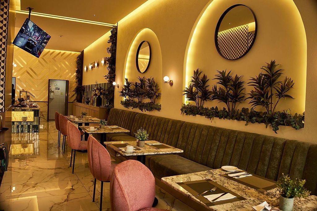 Interior de restaurante cálido y moderno con cabinas curvas, sillas rosas, espejos redondos y faroles colgantes.
