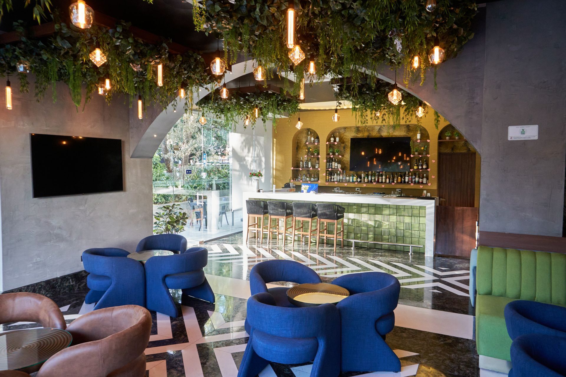 Salón acogedor con sillas azules, luces colgantes, plantas y un bar al fondo.