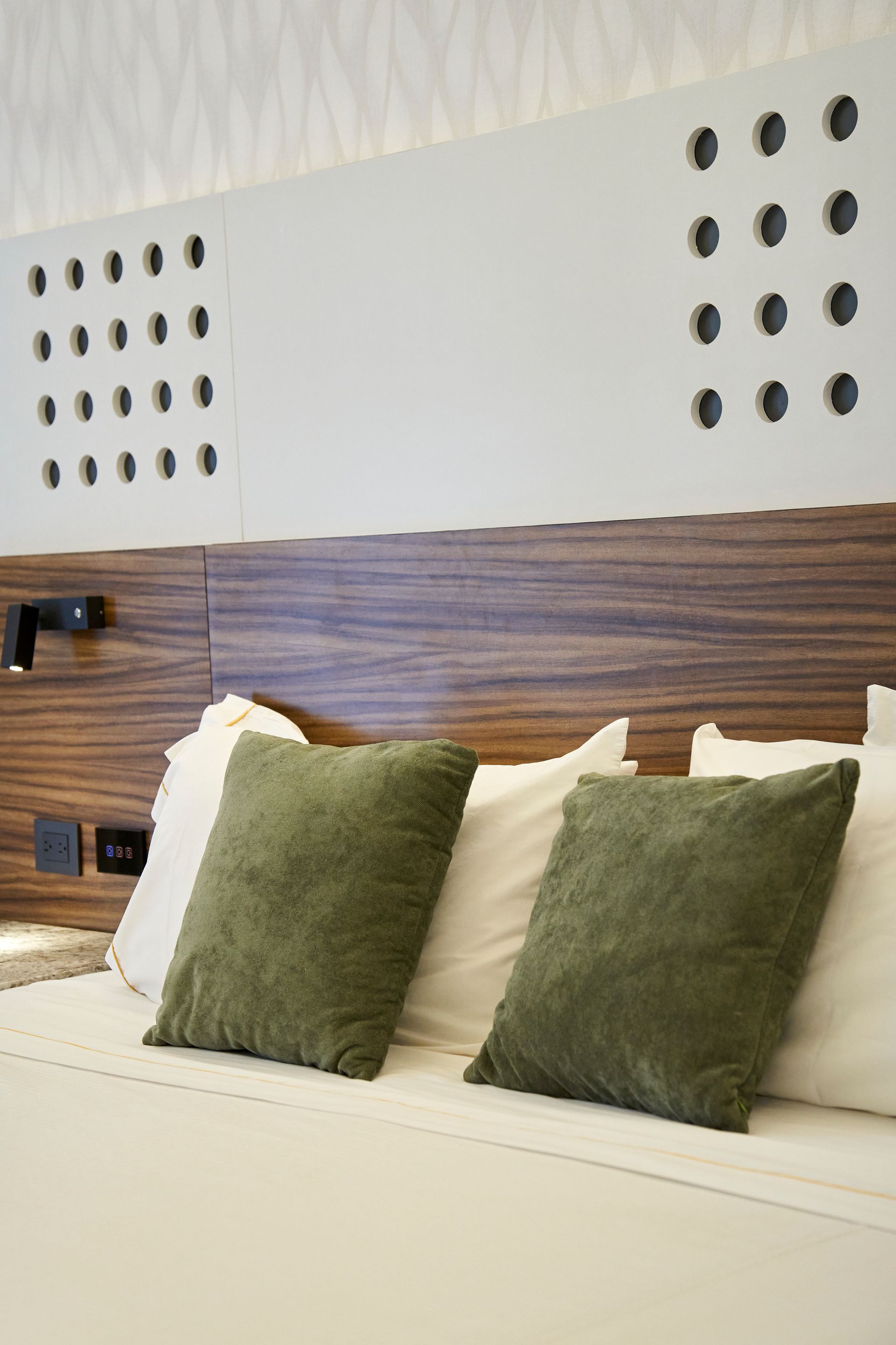 Cama moderna con almohadas verdes, ropa de cama blanca y cabecero de madera en un dormitorio minimalista.