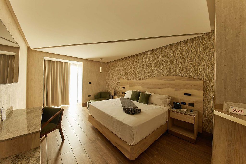 Cama impecable en una habitación moderna con cabecero de madera y elegantes detalles decorativos.