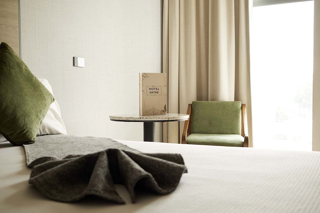 Persona colocando toallas blancas dobladas sobre una cama de hotel en una habitación de tonos cálidos.