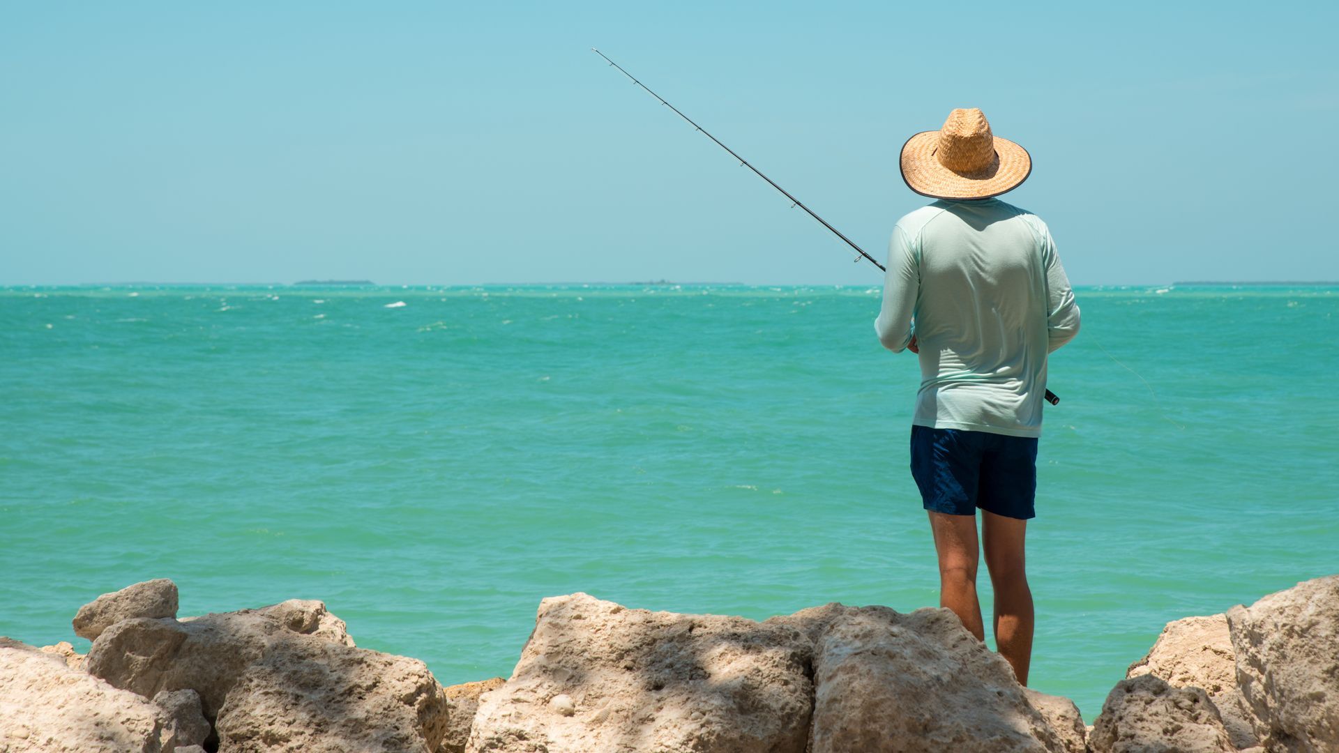 A man in a straw hat is fishing in the ocean.