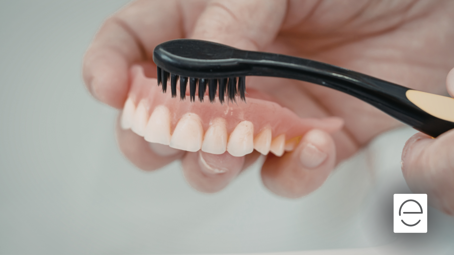 Person brushing dentures with a black toothbrush; close-up.
