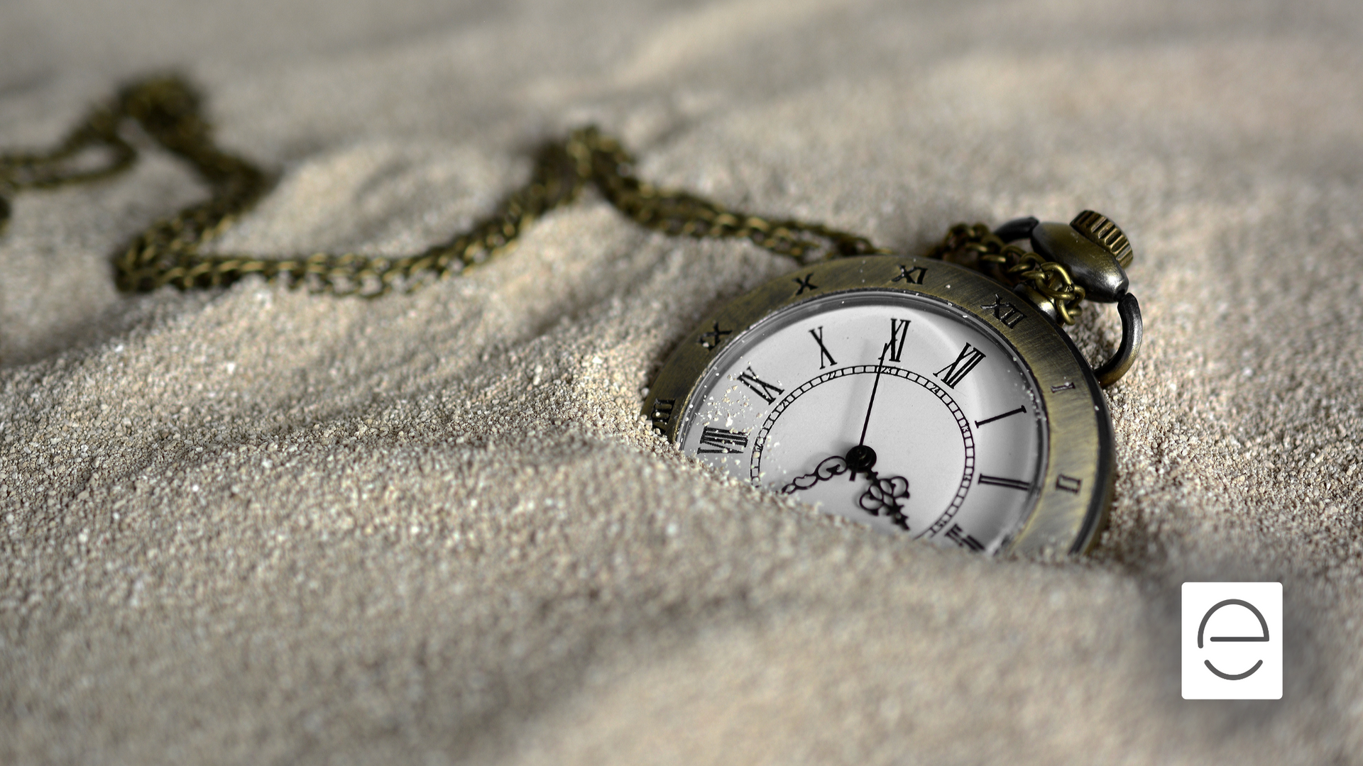 A pocket watch with roman numerals is buried in the sand